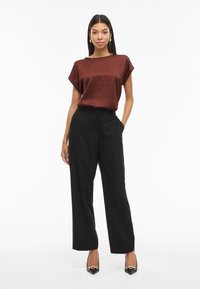 Top corto in satin marrone con maniche corte abbinato a pantaloni neri a gamba larga a vita alta e tacchi neri con un dettaglio dorato.