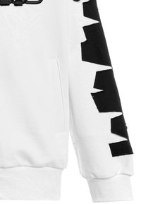 Sudadera blanca con un patrón de zigzag negro en la manga. Incluye un bolsillo lateral y puños de ribete. Textura suave y diseño casual.