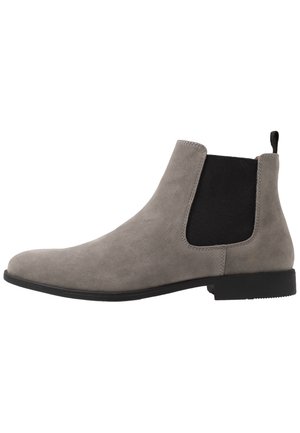 Bottine Chelsea en daim gris avec panneau latéral élastique noir, languette au talon et semelle basse noire, vue de côté extérieur.