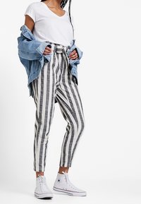 Spodnie w paski o wysokim stanie w czerni i bieli, zestawione z białym t-shirtem i dżinsową kurtką. Białe trampki z wysoką cholewką dopełniają stylizację.