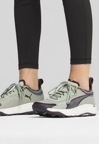 Light green athletic shoes with textured fabric, dark purple accents, and grey soles. Features include laces and branding on the side.
