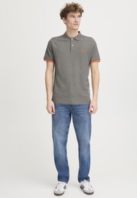 Grå polo shirt med orange detaljer på ærmerne, to knapper og et lille logo på brystet. Båret med lyseblå jeans og hvide sneakers.