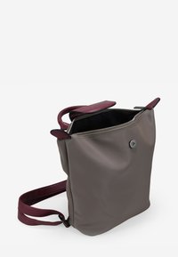 Bolso sintético gris con asas de cuero burdeos. Cierre de cremallera en la parte superior y botón a presión magnético. Textura suave con características de diseño mínimas.