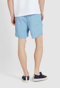 Niebieskie szorty kąpielowe z tylną kieszenią i bocznymi rozcięciami, w połączeniu z granatowymi trampkami i białą koszulą. Gładka tekstura, lekka konstrukcja.