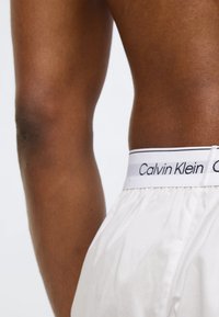 Άσπρα βαμβακερά μποξεράκια με ελαστική μέση, διακοσμημένα με μαύρη επιγραφή "Calvin Klein" και με ομαλή υφή.