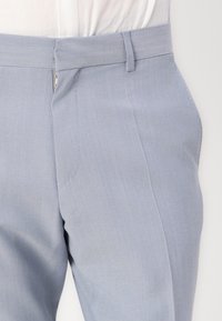 Pantalones azules claros de tela suave con un corte ajustado, que presentan un frente plano, cinturilla con trabillas y un detalle de cremallera lateral.