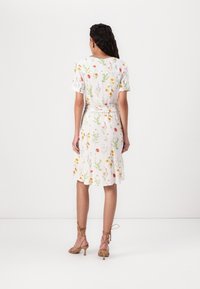 Vitt klänning med blommönster, korta ärmar, ett bälte i midjan och knälång fåll, kombinerad med smala, nakna klackar.