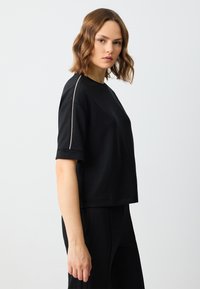 Czarna koszulka z krótkim rękawem, wykonana z miękkiego materiału, z okrągłym dekoltem i podwiniętymi rękawami, z delikatnym, jasnym akcentem wzdłuż rękawa.