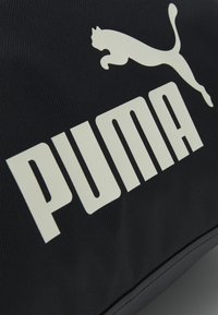 Sort stofpose med et stort hvidt "PUMA" logo og en hvid springende kat-silhuet. Teksturen er glat med subtil ribbning.