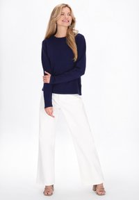 Haut à manches longues côtelé bleu marine associé à un pantalon blanc à jambes larges. Le modèle porte des sandales à talons blocs beige. Design simple et épuré, couleurs neutres.