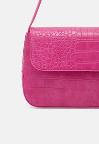 Różowa torebka z eko skóry o fakturze skóry krokodyla. Posiada klapę zapięcia oraz cienki pasek na ramię do noszenia.