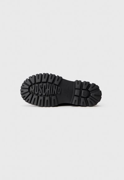 Suela de bota de goma negra con patrones de relieve profundos; presenta el nombre de la marca "MOSCHINO" en relieve; diseño plano adecuado para tracción y durabilidad.