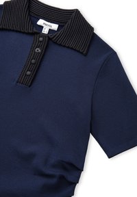 Námořnická modrá polo košile s krátkým rukávem, silným žebrovaným černým límcem a légu s třemi černými knoflíky a jedním dekorativním knoflíkem.