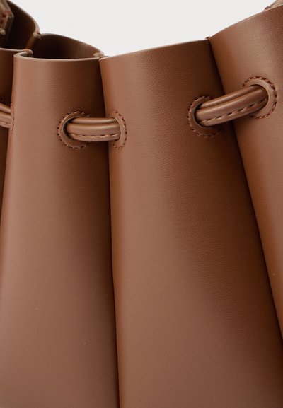 Λεπτομέρεια καφέ δερμάτινης τσάντας που δείχνει ραμμένους θηλιές με δερμάτινα κορδόνια περασμένα για κλείσιμο.