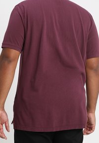 T-shirt bordeaux à manches courtes, fabriqué en coton doux. Il présente un col rond et un ourlet droit, avec des détails de couture visibles.