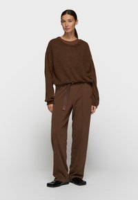 Pull ample marron à manches longues, en matière douce, associé à un pantalon marron ample avec ceinture et détail discret du logo.
