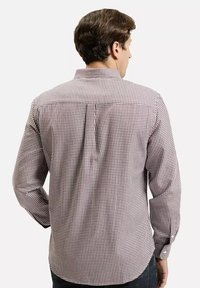 Mężczyzna odwrócony plecami, ubrany w czerwoną i białą koszulę w małą kratkę z długim rękawem oraz ciemne spodnie.