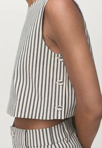 Gestreifter Leinen-Croptop in Creme und Marineblau, mit ärmellos Design und drei runden Knopfakzenten entlang der Seitennaht.