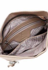 Interiér tašky z látky v béžové barvě s kapsou na zip, několika přihrádkami a textovým vzorem. Viditelné prvky ze stříbrného kovu.