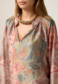 Bluză cu model floral în culori pastelate—roz, albastru și galben. Material moale cu decolteu în V și detalii pliate la umeri. Colier statement aurie.