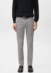 Pantaloni grigio chiaro a taglio slim, realizzati in tessuto liscio, con vita standard e tasche frontali. Abbinati a mocassini neri.