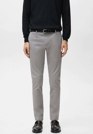 Pantalones gris claro de corte slim, confeccionados en tela lisa, con cinturilla estándar y bolsillos frontales. Combinados con mocasines negros.