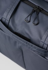 Dunkelblauer Rucksack aus glattem, strukturiertem Stoff, mit einer mit Reißverschluss verfügbaren Tasche und einem kleinen Klettverschluss-Patch. Doppelter Reißverschluss für einfachen Zugriff.