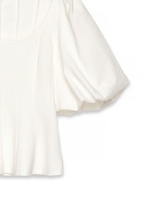 Blusa bianca con maniche a sbuffo, caratterizzata da un collo rotondo, pannelli strutturati e una morbida texture del tessuto con una vestibilità rilassata. Cuciture decorative visibili.