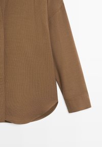 Brown long-sleeve shirt with a textured fabric, featuring a rounded hem and cuffs. The design is simple and modern with a relaxed fit.