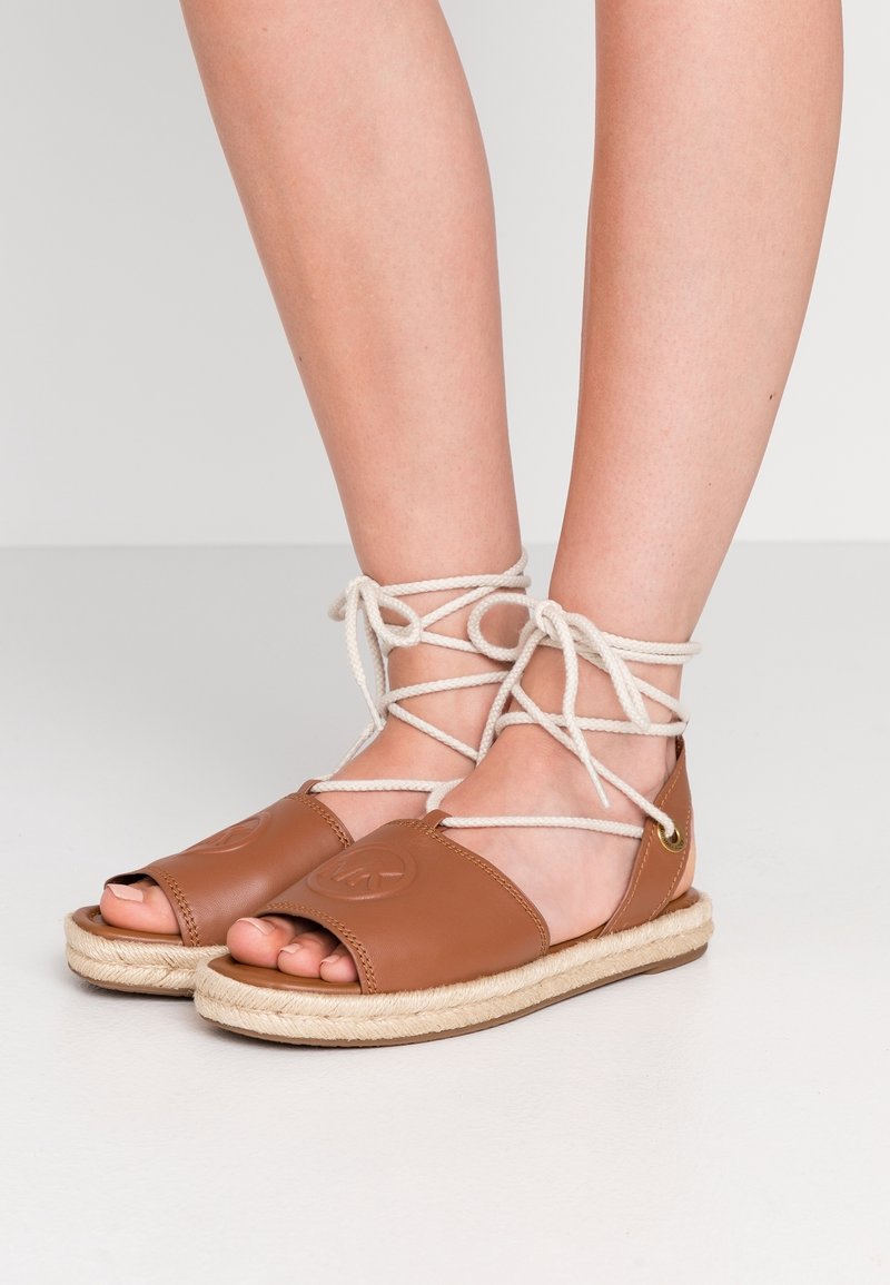 Sandales en cuir marron avec bouts ouverts, dotées d'une semelle en jute tissée et de lacets beige croisés autour des chevilles.