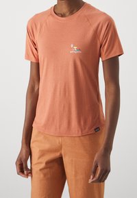 Camiseta de manga corta y cuello redondo en tejido de color naranja coral con textura suave; presenta un logo multicolor de Patagonia en el frente.