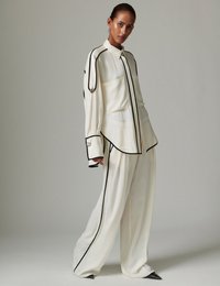 Λευκή, ρέουσα μπλούζα και παντελόνια με φαρδιά μπατζάκια και μαύρη επένδυση. Η μπλούζα διαθέτει τσέπη, ενώ τα παντελόνια έχουν χαρακτηριστικό αιχμηρό τελείωμα.