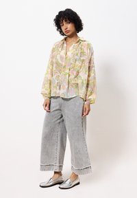 Blouse à manches longues en tulle à motifs floraux aux couleurs pastel ; associée à un jean large gris et des mocassins argentés à texture lisse.