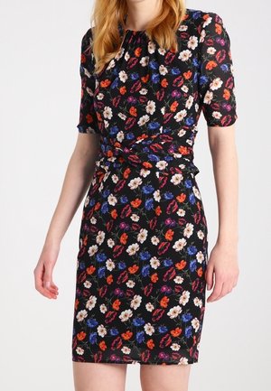 Woman wearing a knee-length black dress with red, white, purple, and blue floral patterns and short sleeves.