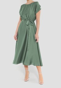 Grön satin midi-klänning med korta ärmar, insydd midja och knytbälte. Flödande silhuett med en mjuk textur och ankellång fåll.