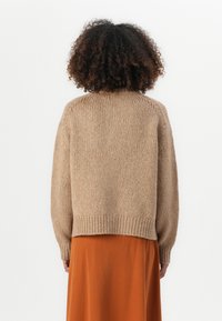 Beige strikket genser med avslappet passform, ribbede mansjetter og nederkant, strukturert mønster, kombinert med en oransje flytende skjørt. Vist fra baksiden.