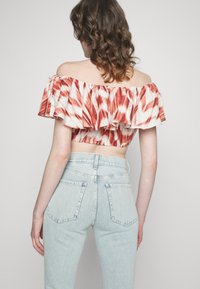 Top cropped em vermelho e branco, com mangas com ondas, usado com calças de ganga de cintura alta em azul claro, com bolsos nas costas e costuras.