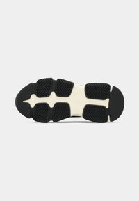 Semelle extérieure en caoutchouc noir et blanc d'une basket avec des motifs de bande de roulement segmentés pour l'adhérence et la flexibilité.