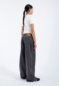 Wide-leg, gray denim jeans with a high waist and belt loops. Features stitched back pockets and a leather patch on the waistband.