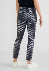 Marineblauwe broek met een geometrisch hartpatroon in roomwit en kastanjebruin. Smal model met een soepele textuur, voorzien van achterzakken en een cropped lengte.