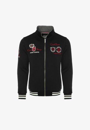 Zwarte trui met ritssluiting en een hoge kraag. Voorzien van rode en witte geborduurde logo's op de borst en mouwen. Geribbelde manchetten en zoom met strepen.