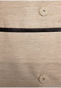 Canvasväska med en texturerad beige yta, som har ett mörkbrunt läderhandtag och två knappar. Enkel design med funktionella detaljer.