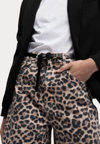 Džínové kalhoty s leopardím potiskem a černým páskem se zlatou sponou. Nosené s bílým tričkem a černým blejzrem. Viditelná strukturovaná tkanina.