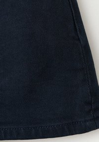 Gros plan d'un tissu en denim bleu foncé avec un tissage diagonal visible et des coutures cousues le long des bords.