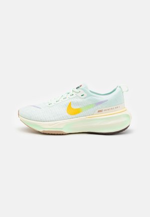 Lys grøn Nike Invincible Run 3 løbesko med gul og lilla swoosh, støddæmpende sål og snørelukning på hvid baggrund.