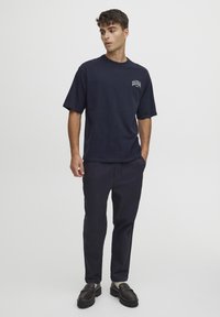 Marineblå bomuld t-shirt med korte ærmer og rund hals, med et lille logo på brystet; parret med mørke bukser og sorte sko.
