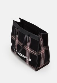 Svart väska med ett strukturerat rutig mönster i röd och vit. Utrustad med robusta svarta handtag och en vit logotyp på framsidan. Öppen toppdesign.