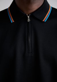 Gros plan d'un polo noir avec fermeture éclair et col présentant des rayures bleues, rouges et jaunes sur une personne.