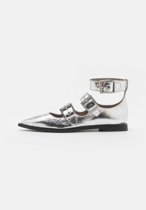 Zapato plano plateado brillante con punta puntiaguda y tres correas con hebilla, incluyendo una correa ancha en el tobillo, sobre una suela negra contra un fondo blanco.