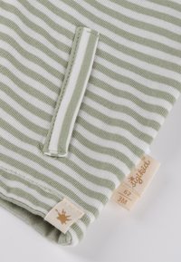 Grün-weiß gestreifter Stoff mit einer Taschenverzierung. Verfügt über ein Etikett mit goldfarbenem Akzent. Weiche Textur, für Säuglinge gedacht. Größe 3 Monate.